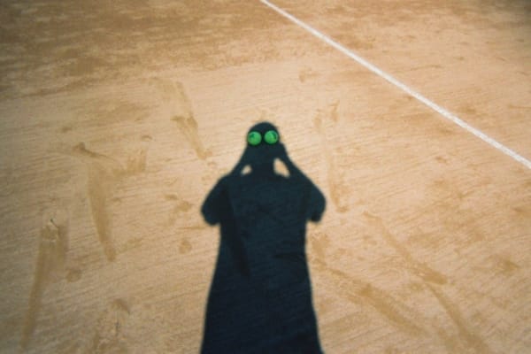 A shadowy figure stands on a sandy field.